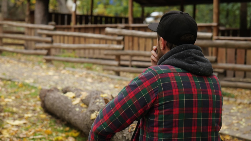 back view. Outdoor a man in a cap with a beard drinks Chinese tea from a bowl