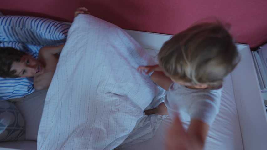 Child jumping into bed. Happy siblings covering under duvet sheets