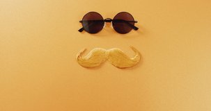 Video of blonde false moustache and round sunglasses on yellow background. Father's day, dressing up, party props, fun and celebration concept.