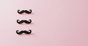 Video of three black false moustaches on pink background with copy space. Father's day, dressing up, party props, fun and celebration concept.