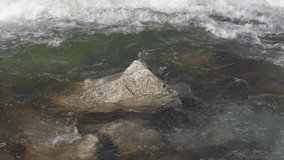 Water flowing in spring river over small rock, slow motion video