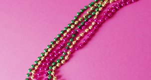 Video of pink, gold and green mardi gras carnival beads on pink background. Carnival, dressing up, party props, fun and celebration concept.