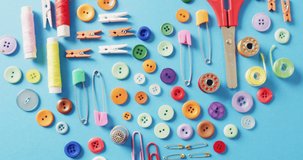 Video of scissors, buttons, pins, clips, pegs and cotton reels in a heart shape on blue background. Sewing, dressmaking, creativity, crafts and hobbies concept.