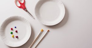 Video of paper plates with paint, paintbrushes and scissors on white background with copy space. Art, painting, creativity, crafts and hobbies concept.