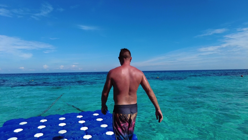 A man jumping from a pier, a man doing a backflip from a pontoon in the tropics
