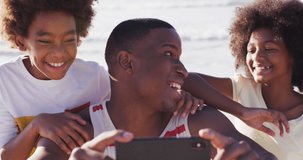 Animation of christmas confetti over african american family taking selfie on beach. Christmas, tradition, celebration and festivity concept digitally generated video.