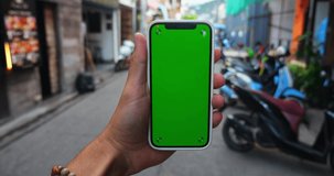 Man's hand holding smartphone with green screen chroma key outdoors on urban city street background, close-up.