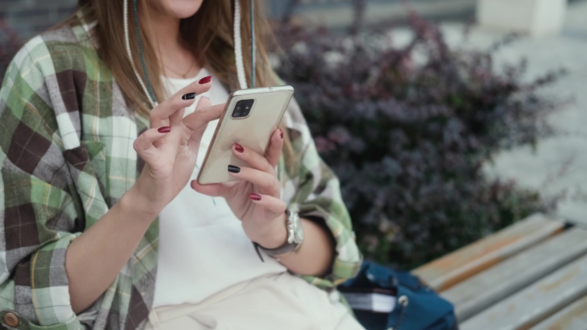 A woman in a hat holds a mobile phone in her hands while sitting on a bench. Woman blogger subscribes to new social networks, buys online, orders goods online in apps.