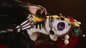 Vertical video: Lady of dead talking on phone call with smartphone, wearing flowers crown and cavalera catrina halloween costume. Woman dressed as santa muerte to celebrate mexican culture holiday