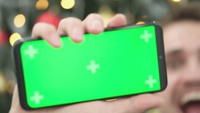 Hand holding smartphone with green screen on Chroma key. Festive winter New Year's decor Christmas tree on a background of Christmas blurred lights background. Promotions, online shopping, business.