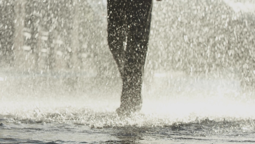 Silhouette of male legs. A girl runs barefoot on the water on a sunny summer day. Water splashes effectively fly to the sides. Depth of field. 