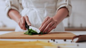 A young chef cuts greens with a white ceramic knife, cooking in a restaurant fast cooking salad cutting greens on a cutting board. Cook in special clothes in home kitchen - Powered by Shutterstock - Get 15% off with code: PIKWIZARD15