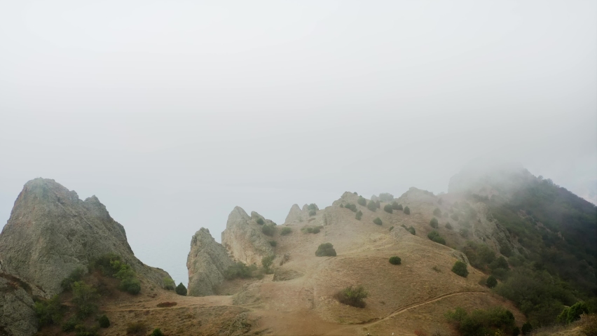 The cliff above the sea, the sharp rocks and stones, the fog obscures the view and overflows the mountain range. Drone aerial shot.