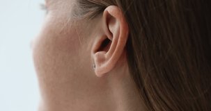 Young woman putting wireless earphone into ear close up. Gadget user lady showing using white small earbud for listening to music, video phone call. Cropped shot