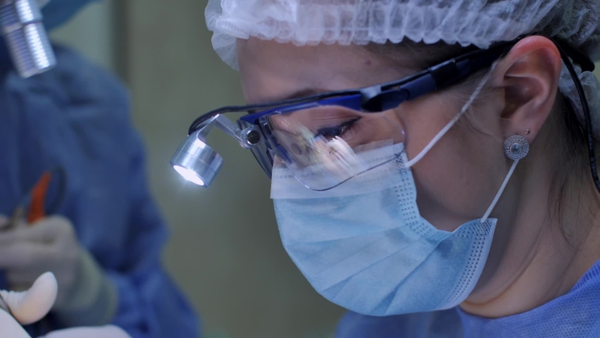 Close-up of a female surgeon face and eyes with safety glasses and surgical headlight, who is doing surgery with determination inside the operating room, concept of health care. - Powered by Shutterstock - Get 15% off with code: PIKWIZARD15