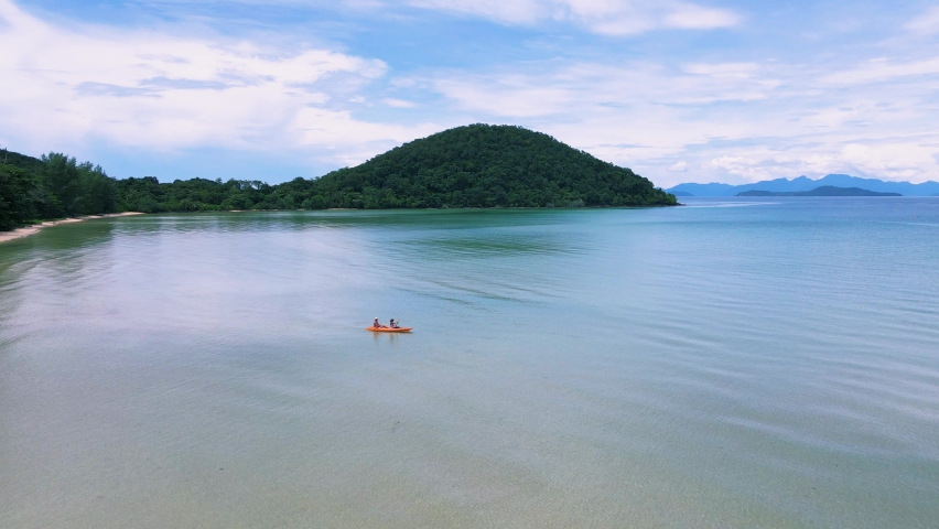 A couple mid age men and women paddling in Kayak in the ocean of the tropical Island of Koh Mak Thailand. men and women in kayaks at a blue ocean and white beach with palm trees
