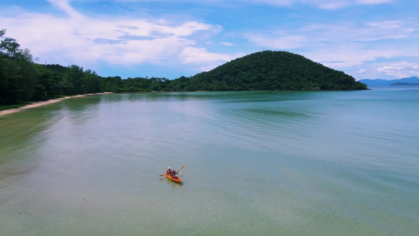 A couple mid age men and women paddling in Kayak in the ocean of the tropical Island of Koh Mak Thailand. men and women in kayaks at a blue ocean and white beach with palm trees