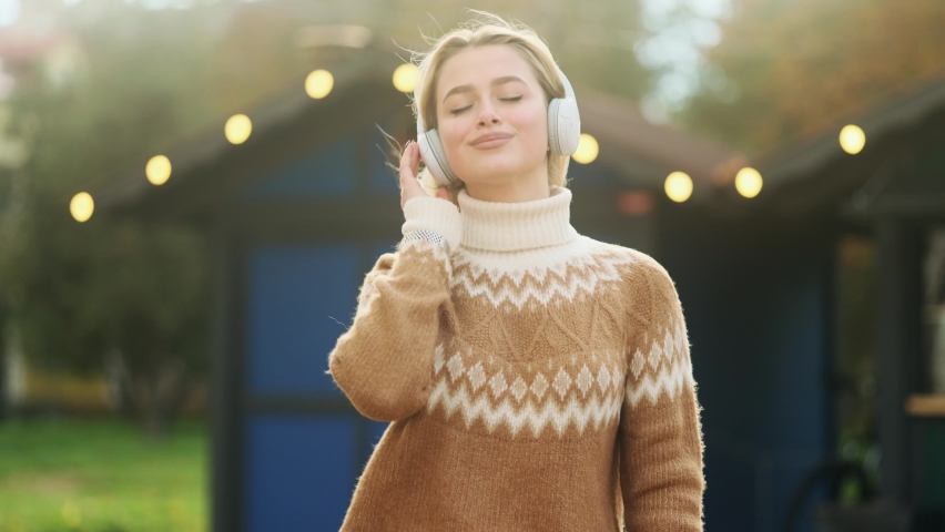 Young charming blond girl enjoying music in the city centre. Gorgeous woman listening to music and dancing in headphones while walking down the street. 
