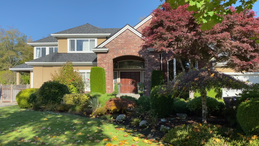 Establishing shot of two story stucco luxury house with garage door, big tree and nice Fall Foliage landscape in Vancouver, Canada, North America. Day time on Sept 2022. ProRes 422 HQ.