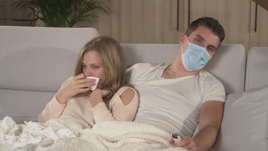 CLOSE UP: Husband comforting his coughing sick wife while she is having a flu. Winter colds and viruses spreading around. Married couple cuddling on comfy couch while woman is having seasonal virus. Royalty-Free Stock Footage #1096453119