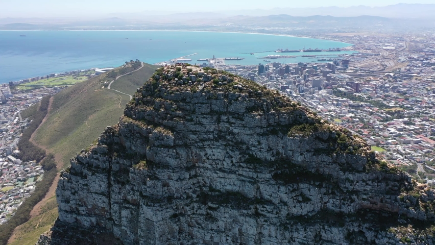 Aerial video view - flying around the peak of Lion's Head mountain in Cape Town, South Africa, with a view of Downtown Cape Town,  Seaport, Camps Bay and Robben Island - K4 movie 