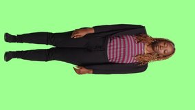 Vertical video: African american woman standing with full body on greenscreen backdrop, acting sleepy and tired. Being exhausted, drained and yawning over green screen isolated chroma key background.