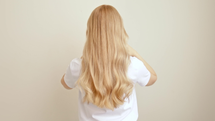 Blonde woman stands with her back throws long wavy hair. The concept of dyeing and hair extensions. Royalty-Free Stock Footage #1096458703