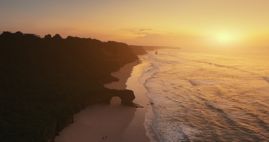 Rock wall on sand beach aerial view. Slow motion sun set ocean waves. Giant hole on cliff sea coast. Wave wash shore cinematic drone shot. Nobody nature summer scenery. Travel Los Angeles, California.