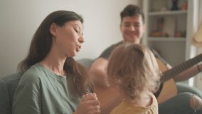 Happy young multiethnic parents and their toddler son spend time together and play guitar at home. Woman, man and a kid sitting on sofa and smiling. Music family and creativity concept. Couple in love - Powered by Shutterstock - Get 15% off with code: PIKWIZARD15