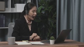 Businesswoman wearing headset and microphone working at her desk and using laptop. Enthusiastic female employee utilizing laptop for remote online meeting, business video conference in the office.