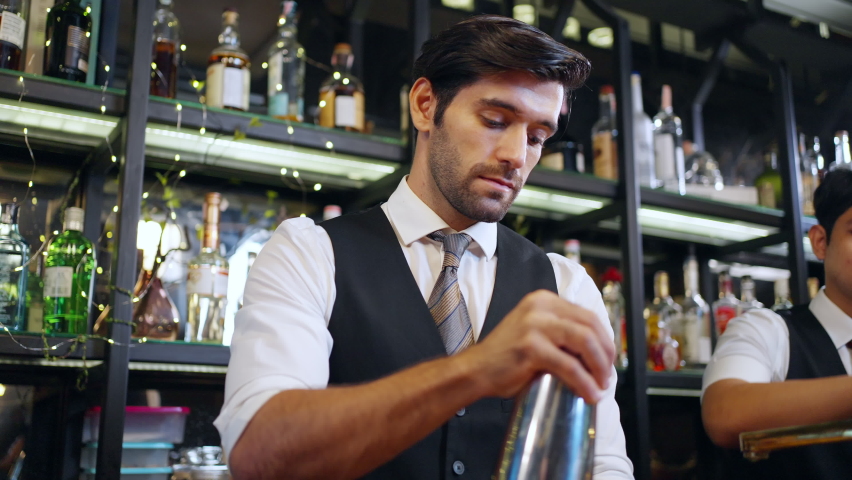 Handsome man bartender preparing cocktail drink in cocktail shaker serving to customer on counter at luxury restaurant bar. Barman making mixed alcoholic drink celebrating holiday party at nightclub Royalty-Free Stock Footage #1096464037