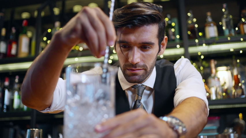 4K Handsome man bartender preparing cocktail drink in cocktail glass serving to customer on counter at luxury restaurant bar. Barman making mixed alcoholic drink celebrating holiday party at nightclub Royalty-Free Stock Footage #1096464055