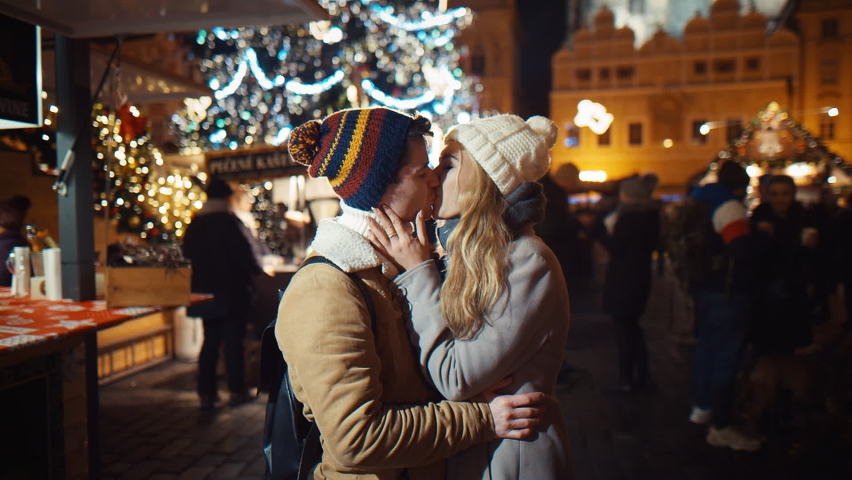 Young woman meeting up with boyfriend and kiss on christmas evening party hugging tightly together swinging under a big Christmas glowing fir tree at a street fair. Concept for Christmas, New Year
