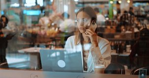 Business woman using mobile phone, dialing, talking with business partners or colleagues about work project, sitting at cafe and telecommuting on laptop. Online business. Freelance Remote work Startup
