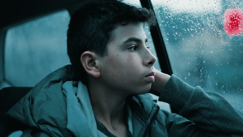 Depressed teen boy seated in car backseat looking out window during rainy day. Sad kid feeling boredom on road Royalty-Free Stock Footage #1096475637