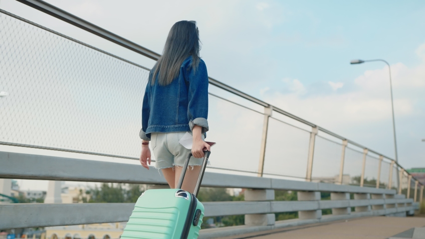 Asian woman traveler walking dragging a suitcase holding a passport and boarding pass. Background sky and airplane Royalty-Free Stock Footage #1096475973