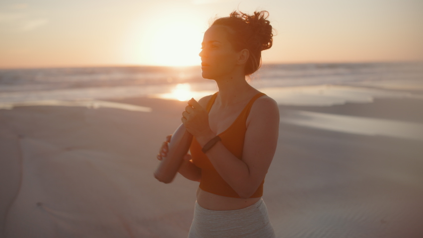 fit sports woman in fitness clothes at the beach in the evening drinking water.