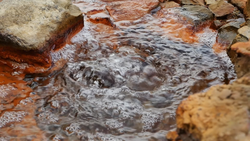 Slow-motion video of bubbling mineral underground source of pure water with bubbles of mineral gases and healthy salts. Red-colored stones around the mineral water geyser. Good for the intestines | Shutterstock HD Video #1096477097