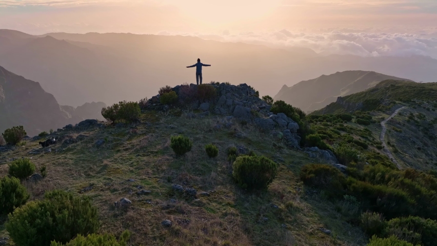 Climber in the mountains achieved his goal and enjoys wonderful nature. Man stands on top of mountain and looks at the sunrise sky. Aerial view of magnificent sunrise in the mountains of Madeira
