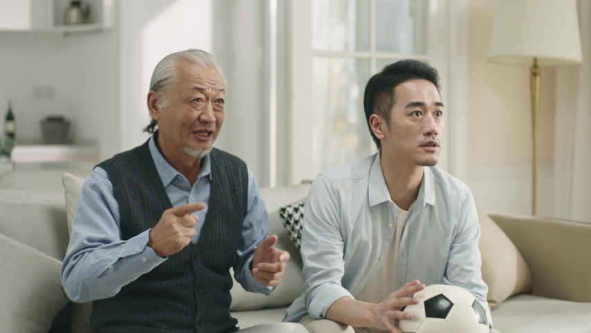 asian senior father and adult son watching live broadcasting of football game on tv together at home and celebrating a goal Royalty-Free Stock Footage #1096486751