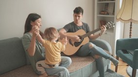 Happy young multiethnic parents and their toddler son spend time together and play guitar at home. Woman, man and a kid sitting on sofa and smiling. Music family and creativity concept. Couple in love - Powered by Shutterstock - Get 15% off with code: PIKWIZARD15