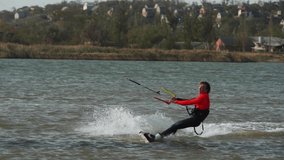 Kiteboarder rides on a kite in sea bay. Freestyle kiter training on pond kiteboarding spot. Kitesurfer enjoying ride. Extreme water sports. Slow motion 120 fps.