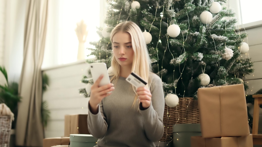 Upset young woman thoughtfully pondering on camera and shrugs while hold phone and credit card. Problem with online order payment error or blocked bank account doing shopping at internet  Royalty-Free Stock Footage #1096491031