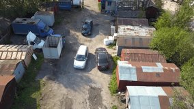 Aerial drone video of car towing with rope another one on a broken road past old rusty garages, trees and ruins outside russian city on a summer sunny day. Help and mutual assistance among motorists.