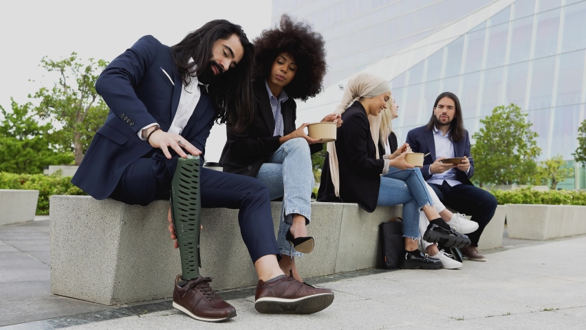 Business man with disability adjusting his prosthetic leg while teamwork having lunch break outside the office