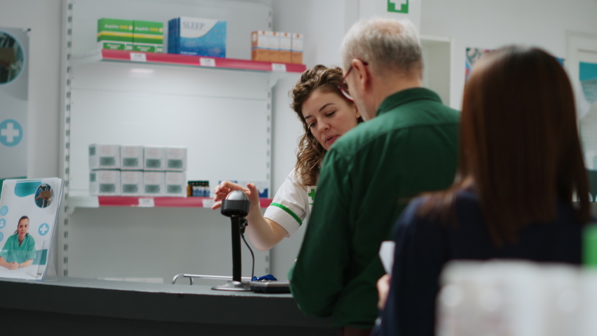 Medical employee serving clients with pills and medicaments, scanning medicine products and giving assistance in pharmacy. Pharmacist helping people to buy treatment and drugs. Handheld shot.