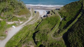 Cinematic 4K Drone video of hidden place by the ocean and sea. In between the cliffs and hills. Small road path and camper car. Beach and waves and little house walking traveling