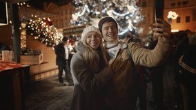 Happy young couple having Christmas date at Old decorated town square. Happy time together, People in love celebrate New Year holidays vacation. Woman and man enjoy Christmas, take selie on smartphone - Powered by Shutterstock - Get 15% off with code: PIKWIZARD15