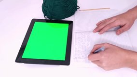 Knitting crochet hobby with tablet PC green screen. Green wool and woman hands making notes in notebook crocheting scheme on desk. Scrolling tab zoom web search app video