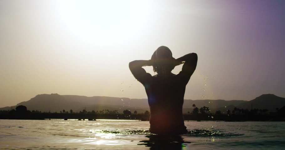 A naked man standing under the sun in the middle of a swimming pool. A view of a handsome bare-chested man standing under the bright sun in the middle of the swimming pool